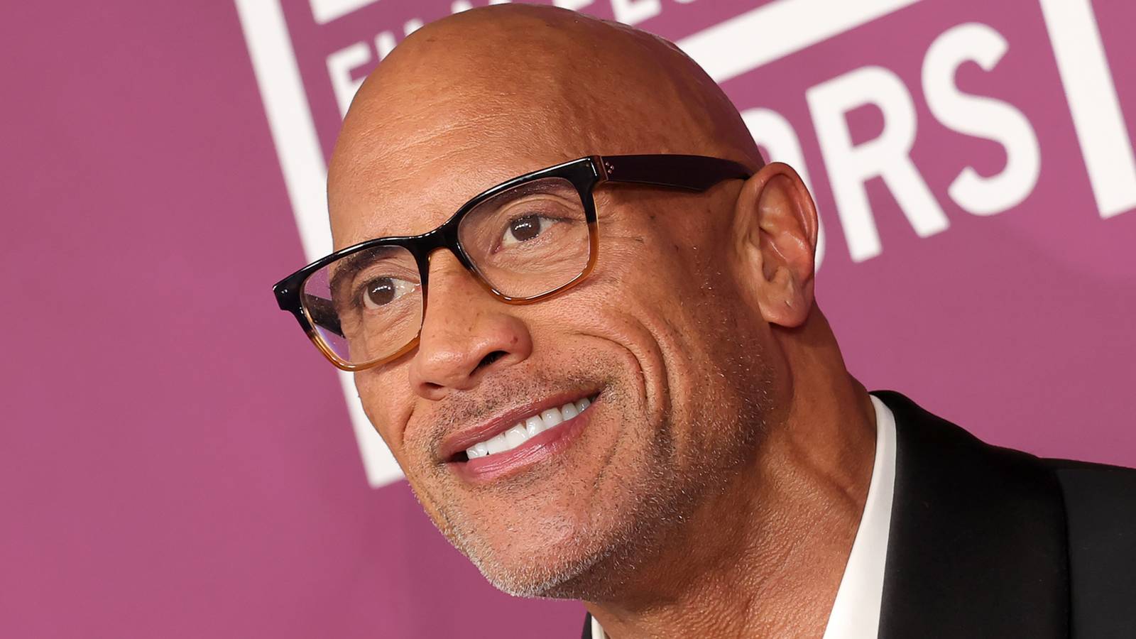 Dwayne Johnson en un evento cinematográfico reciente, con gafas de montura oscura y traje negro
